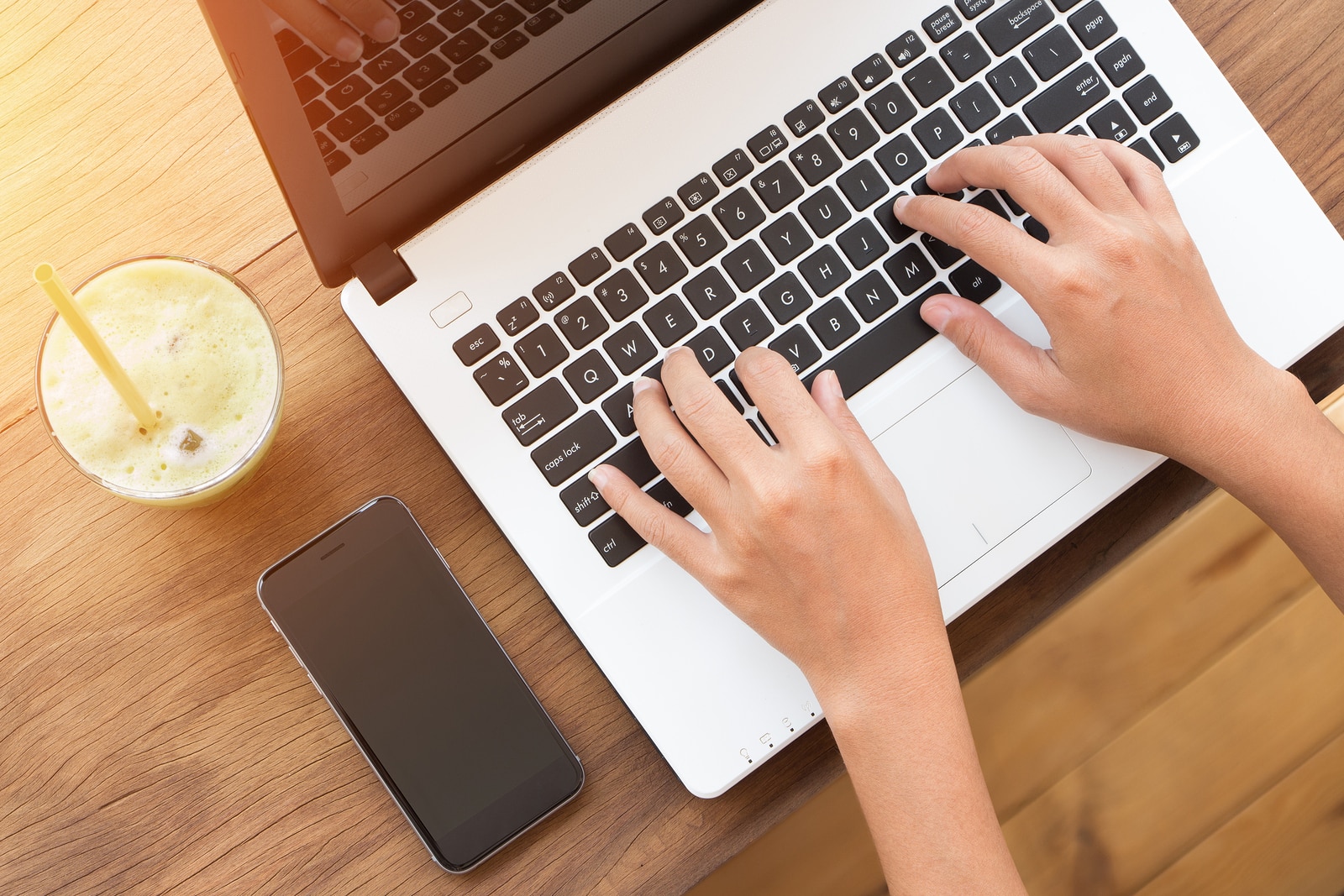 Photo of hands typing on a laptop keyboard, a phone is next to the laptop